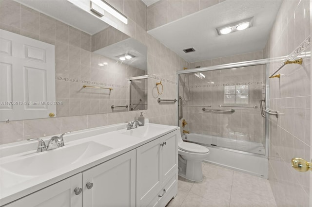 full bathroom with tile walls, tile patterned flooring, enclosed tub / shower combo, vanity, and toilet