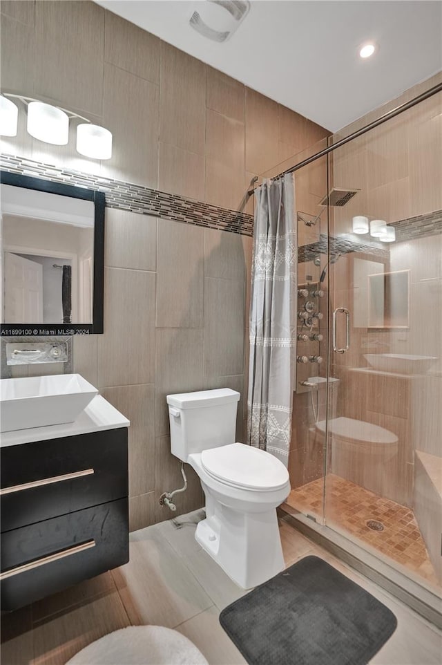 bathroom with tile patterned floors, walk in shower, vanity, tile walls, and toilet