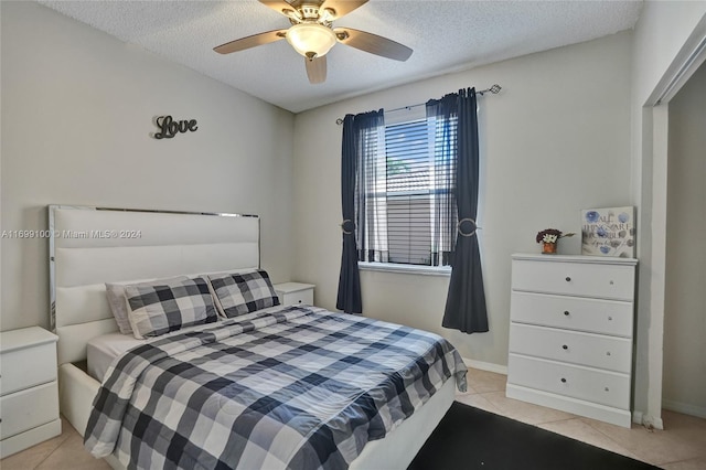 bedroom featuring ceiling fan, light tile patterned floors, and a textured ceiling