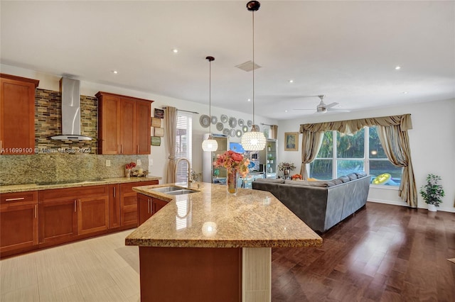 kitchen featuring a kitchen island with sink, ceiling fan, wall chimney exhaust hood, and sink