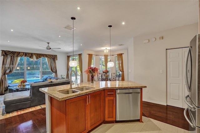 kitchen with appliances with stainless steel finishes, a kitchen island with sink, sink, decorative light fixtures, and light hardwood / wood-style flooring