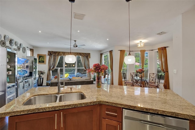 kitchen featuring pendant lighting, sink, ceiling fan, an island with sink, and light stone counters