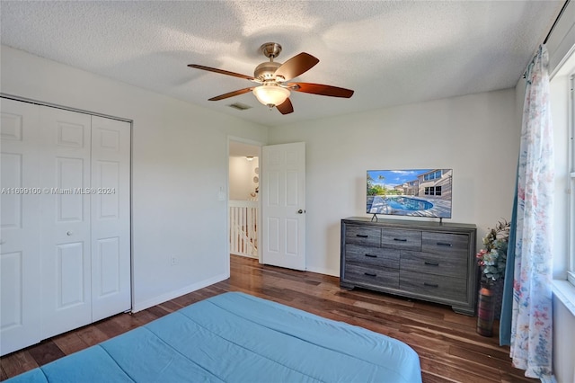 bedroom with a textured ceiling, ceiling fan, dark wood-type flooring, and a closet