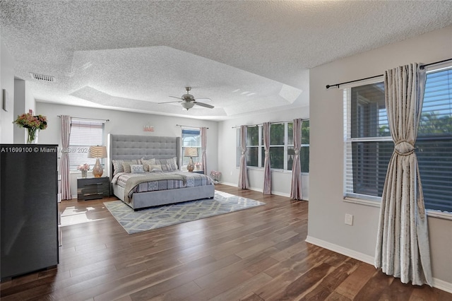 bedroom featuring a tray ceiling, ceiling fan, dark hardwood / wood-style flooring, and a textured ceiling