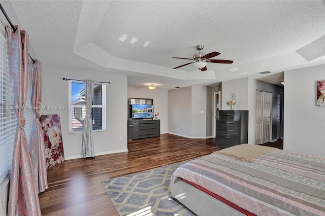 bedroom featuring a raised ceiling, ceiling fan, dark hardwood / wood-style flooring, and a textured ceiling