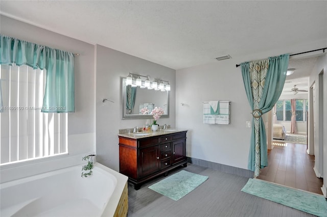 bathroom with a tub to relax in, vanity, a textured ceiling, ceiling fan, and hardwood / wood-style floors