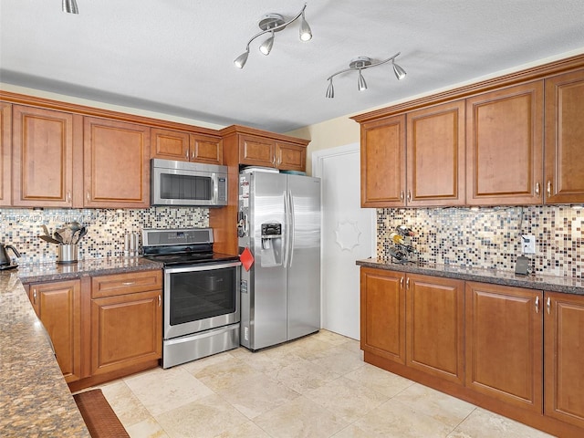 kitchen featuring a textured ceiling, backsplash, appliances with stainless steel finishes, and dark stone counters