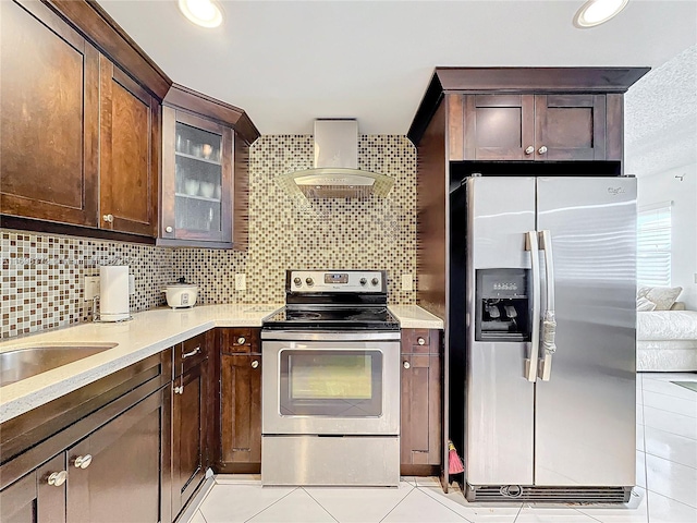 kitchen featuring tasteful backsplash, dark brown cabinetry, wall chimney exhaust hood, and appliances with stainless steel finishes