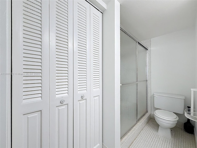 bathroom with tile patterned floors, a shower with door, and toilet