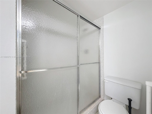 bathroom featuring toilet and a shower with shower door