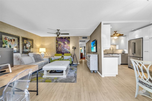 living room featuring a textured ceiling, light hardwood / wood-style floors, ceiling fan, and sink