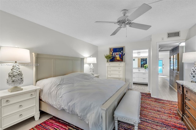 bedroom with a textured ceiling, ensuite bathroom, light hardwood / wood-style flooring, and ceiling fan