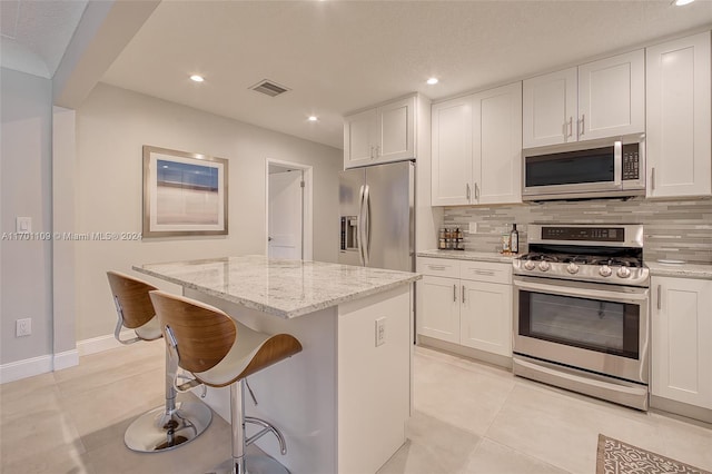 kitchen with light stone countertops, a center island, stainless steel appliances, backsplash, and white cabinets