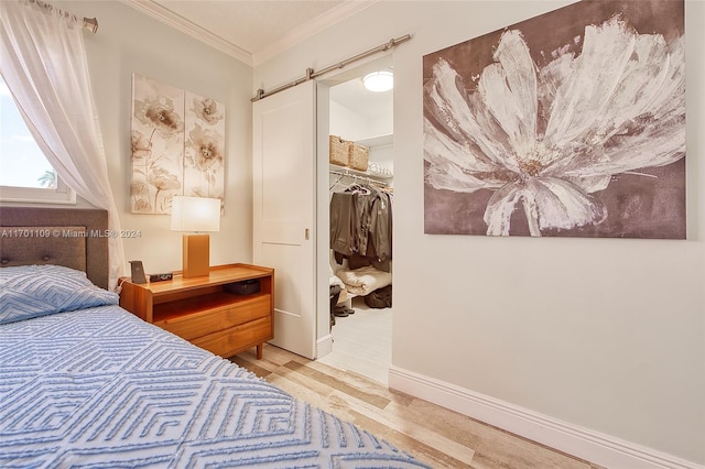 bedroom with a barn door, ornamental molding, light hardwood / wood-style flooring, and a closet