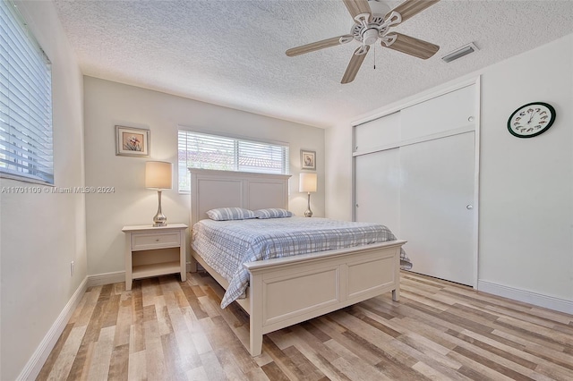 bedroom featuring a textured ceiling, a closet, light hardwood / wood-style flooring, and ceiling fan