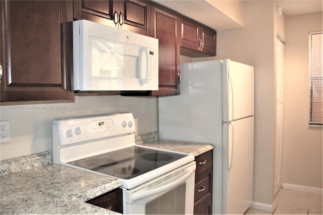 kitchen featuring light tile patterned floors, white appliances, light stone counters, and dark brown cabinetry