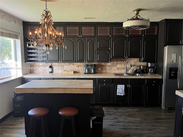 kitchen with sink, dark hardwood / wood-style flooring, stainless steel refrigerator with ice dispenser, a notable chandelier, and backsplash