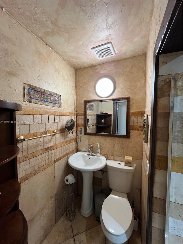 bathroom featuring tile patterned floors, toilet, and tile walls