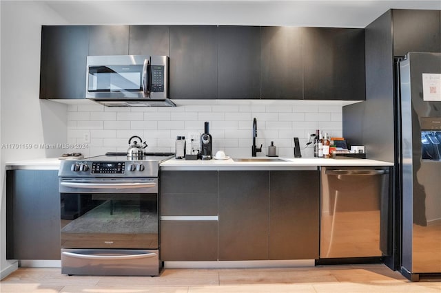 kitchen featuring stainless steel appliances, decorative backsplash, sink, and light hardwood / wood-style flooring