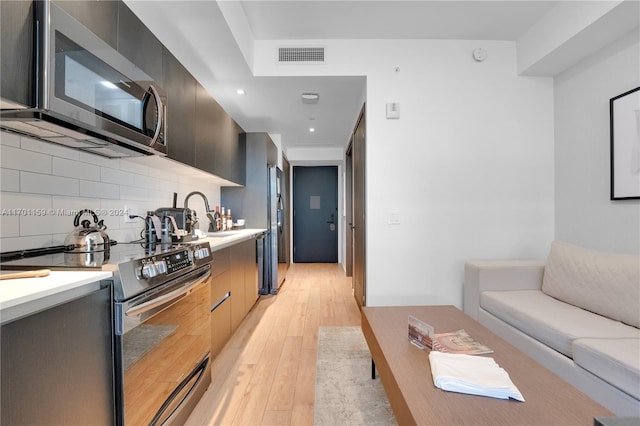 kitchen with stainless steel appliances, decorative backsplash, sink, and light hardwood / wood-style floors