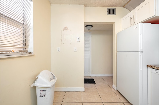 kitchen with a textured ceiling, white cabinets, light tile patterned flooring, and white appliances