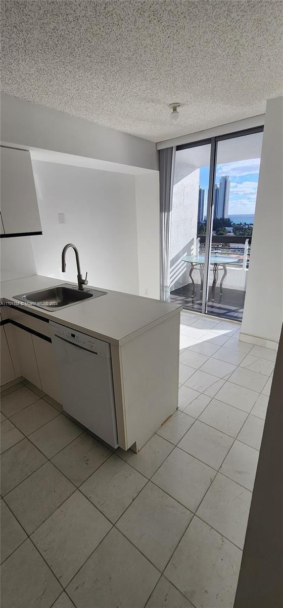 kitchen featuring white dishwasher, sink, light tile patterned floors, a textured ceiling, and white cabinetry