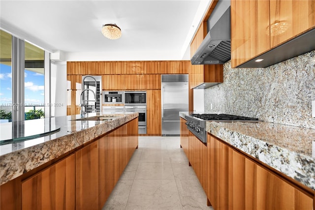 kitchen with exhaust hood, sink, built in appliances, light stone countertops, and tasteful backsplash