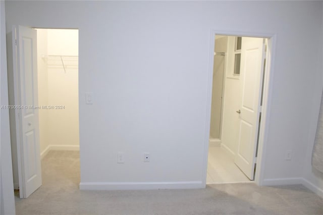 unfurnished bedroom featuring a closet, light colored carpet, a walk in closet, and ensuite bath