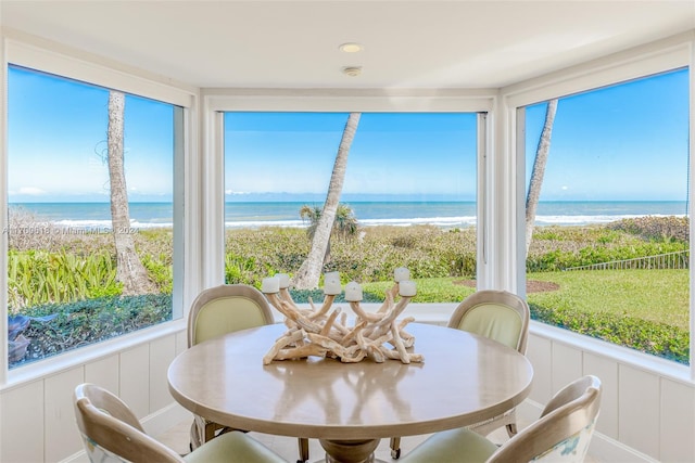 sunroom featuring a view of the beach, a water view, and a wealth of natural light