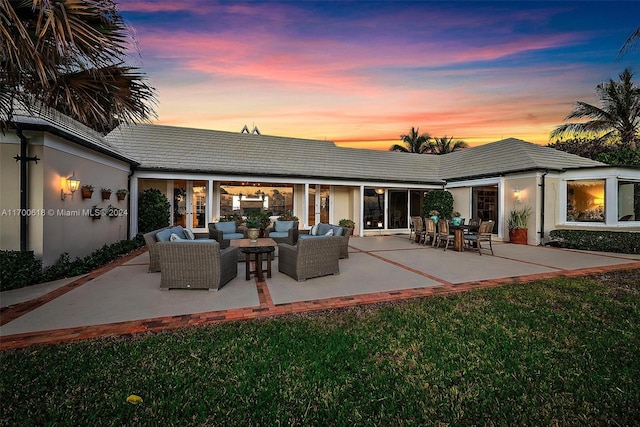 back house at dusk featuring outdoor lounge area, a patio, and a lawn