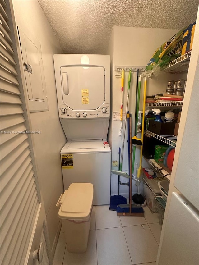 clothes washing area with light tile patterned floors, a textured ceiling, electric panel, and stacked washer and clothes dryer