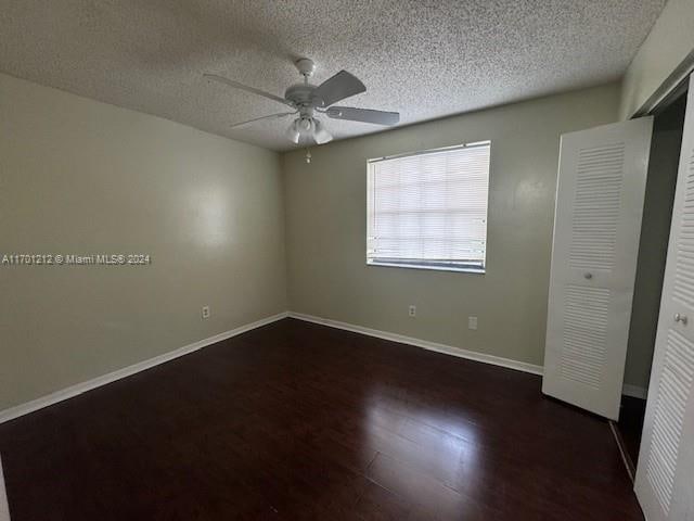 unfurnished bedroom featuring a textured ceiling, a closet, dark hardwood / wood-style floors, and ceiling fan