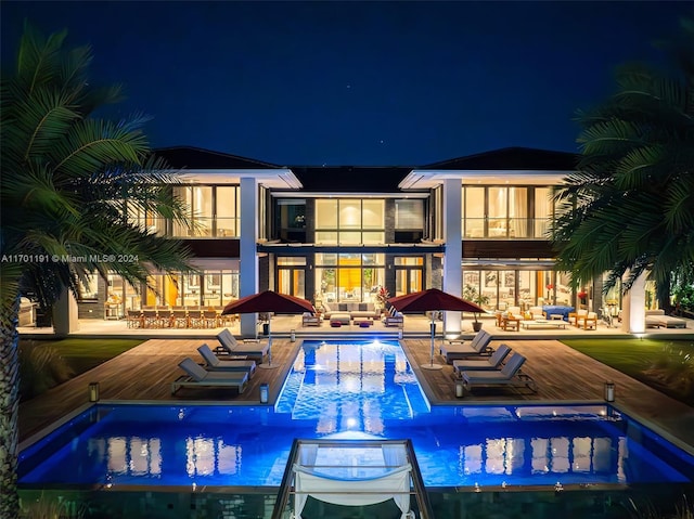 back house at twilight featuring a pool with hot tub