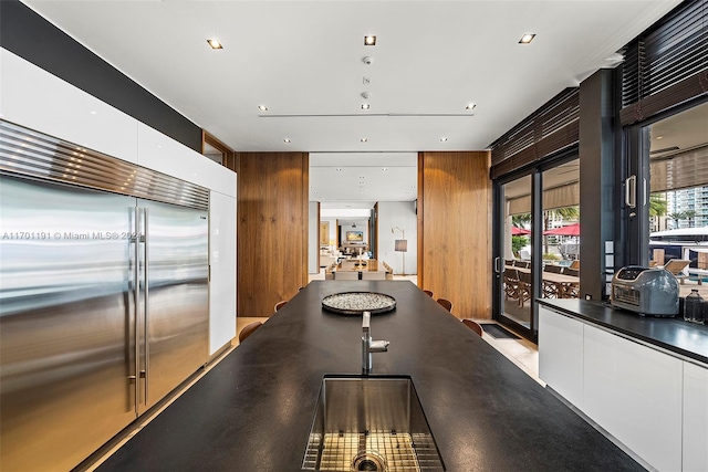 interior space featuring white cabinetry, wooden walls, and stainless steel built in refrigerator