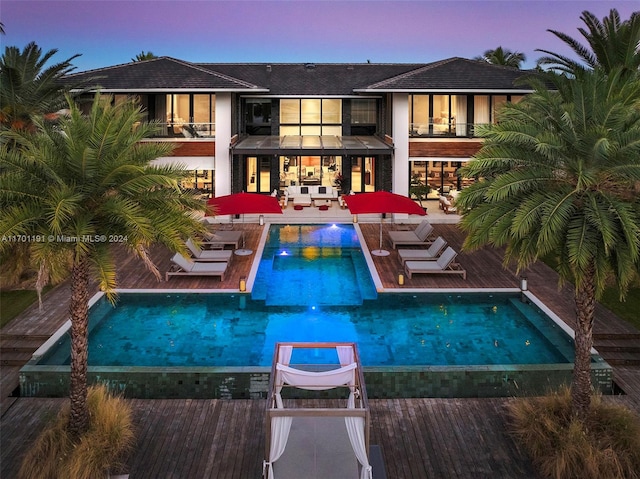 back house at dusk featuring an outdoor living space, a balcony, pool water feature, and a patio