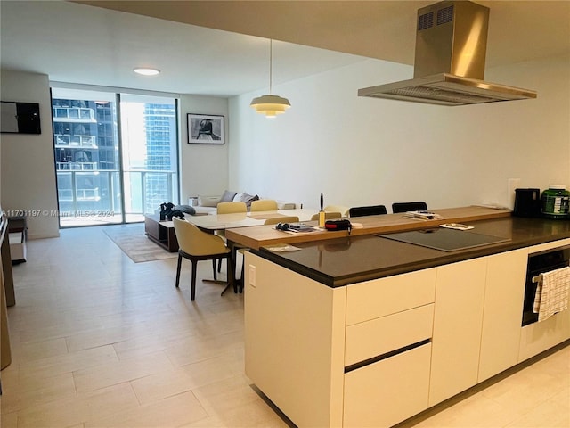 kitchen featuring expansive windows, island range hood, black electric cooktop, decorative light fixtures, and white cabinets