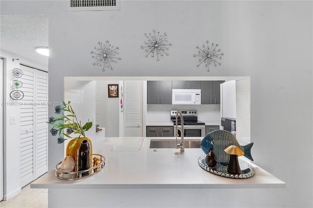 kitchen featuring kitchen peninsula, stainless steel range with electric stovetop, gray cabinetry, a textured ceiling, and sink