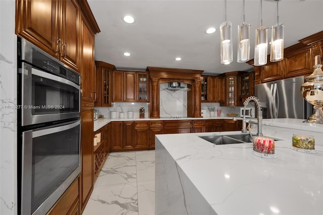 kitchen with sink, tasteful backsplash, light stone counters, decorative light fixtures, and appliances with stainless steel finishes