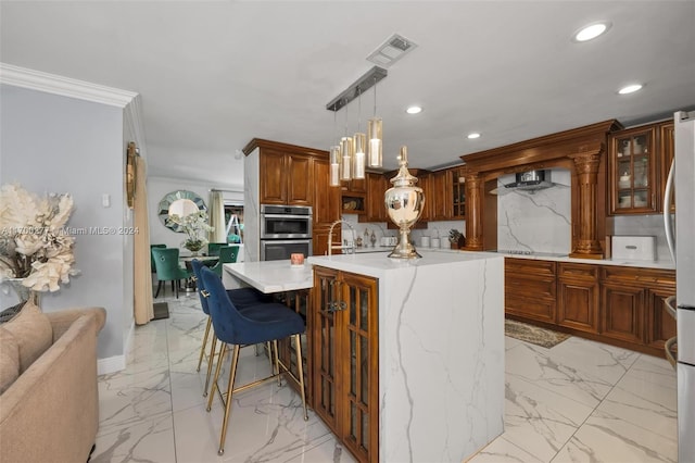 kitchen with a kitchen breakfast bar, ornamental molding, double oven, decorative light fixtures, and a center island with sink