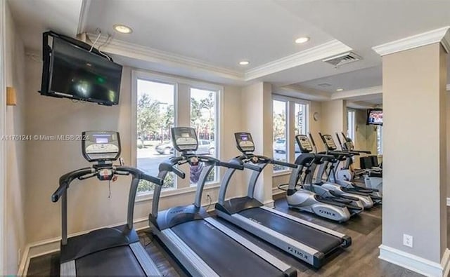 workout area with a raised ceiling, dark wood-type flooring, and ornamental molding