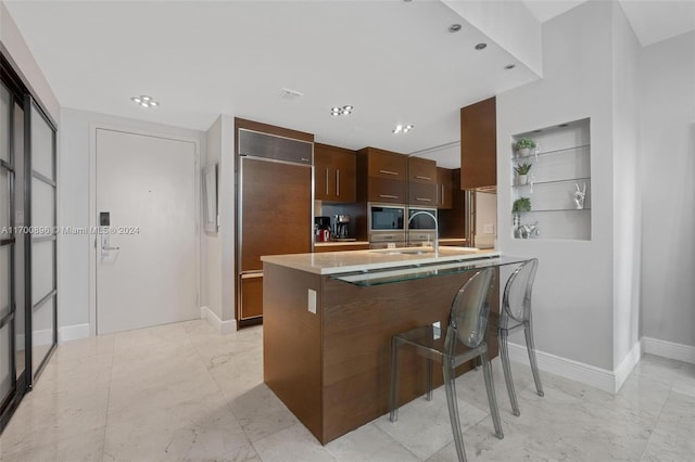 kitchen with sink, built in appliances, built in shelves, a kitchen bar, and kitchen peninsula