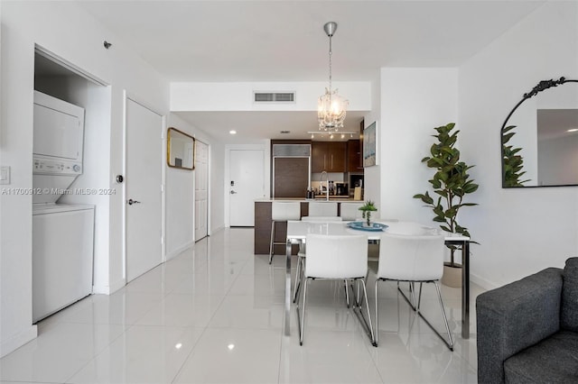 dining room featuring sink, light tile patterned flooring, stacked washer and clothes dryer, and an inviting chandelier