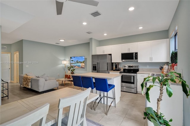 kitchen with a kitchen bar, appliances with stainless steel finishes, a kitchen island, ceiling fan, and white cabinetry