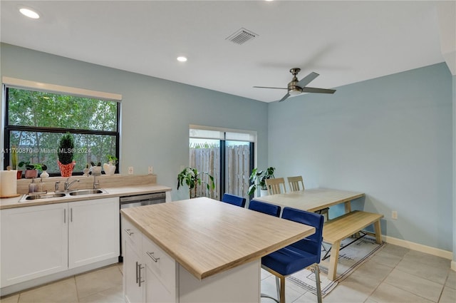 kitchen featuring light tile patterned flooring, white cabinets, sink, ceiling fan, and a kitchen island