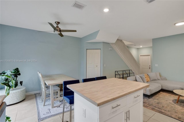 kitchen featuring ceiling fan, a kitchen island, light tile patterned flooring, a kitchen bar, and white cabinets