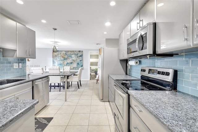 kitchen with light stone countertops, hanging light fixtures, decorative backsplash, light tile patterned floors, and appliances with stainless steel finishes