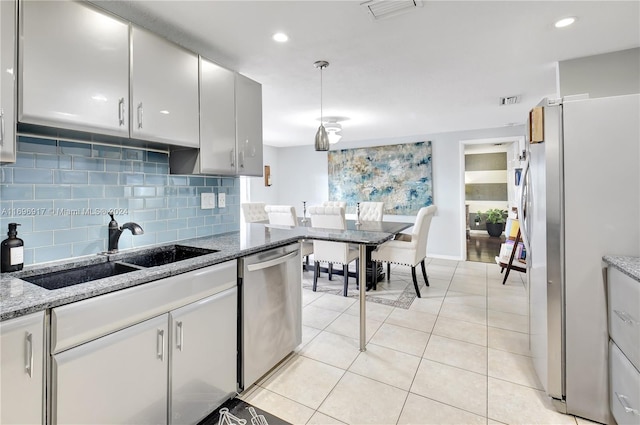 kitchen featuring backsplash, stone counters, sink, light tile patterned flooring, and stainless steel appliances