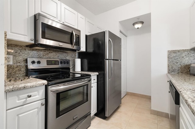 kitchen with light stone countertops, appliances with stainless steel finishes, backsplash, white cabinets, and light tile patterned flooring