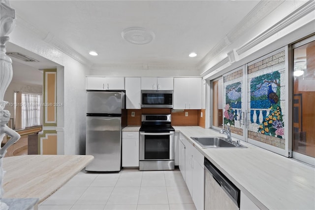 kitchen with appliances with stainless steel finishes, ornamental molding, sink, light tile patterned floors, and white cabinets