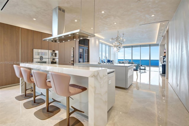 kitchen featuring stainless steel double oven, a spacious island, decorative light fixtures, island range hood, and a water view